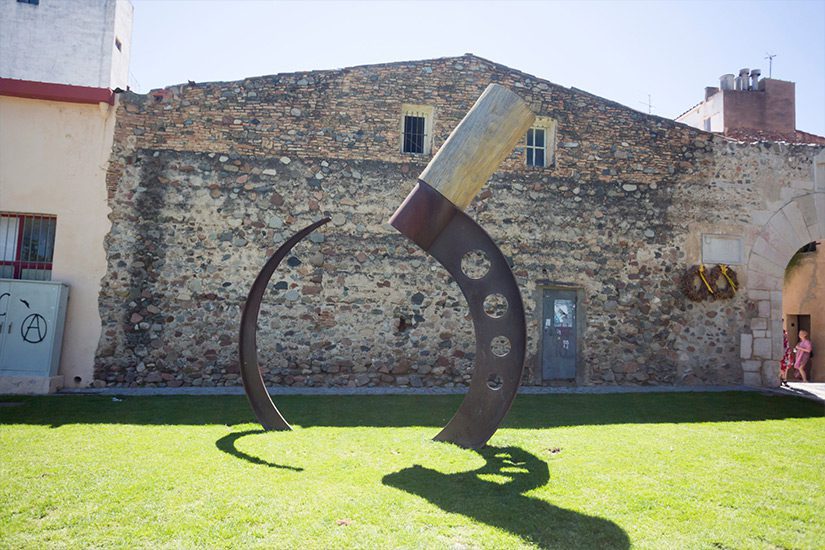 Große Mondsichelskulptur vor der Kulisse einer alten Stadtmauer Cambrils